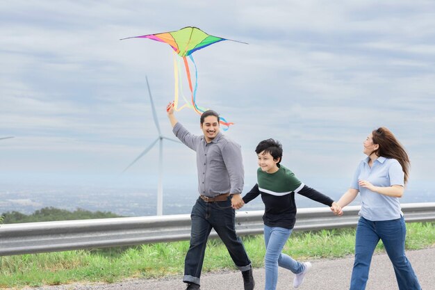 Progressives, glückliches, sorgloses Familienurlaubskonzept, fliegender Drachen mit Windkraftanlage