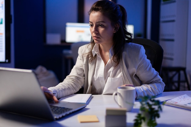 Projektmanager, der spät in der Nacht online mit Kollegen spricht, die auf einem professionellen Laptop im Geschäftsbüro sitzen