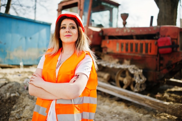 Projete a mulher do construtor no colete uniforme e no capacete protetor alaranjado contra a escavadora.