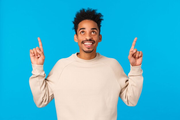 Promoção maravilhosa. Espantado, animado sorrindo feliz homem afro-americano com corte de cabelo afro hipster, bigode, olhando para cima admirando a vista, encontrou um excelente presente para o dia dos namorados, azul