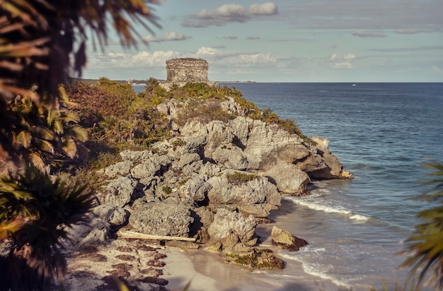 Promontorio rocoso con vista al Mar Caribe con un antiguo edificio maya en la parte superior: Atalaya del complejo maya de Tulum en México.