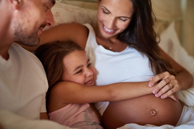 Y pronto habrá cuatro Tomas de una niña feliz acostada en la cama con su papá y su madre embarazada