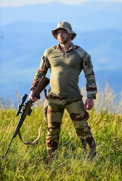 Pronto para atirar. Forças do exército. Roupa militar de homem com arma. Foco e concentração caçador experiente. Guerreiro brutal. Rifle para caça. Hunter segura o rifle. Fundo de paisagem de montanhas Hunter.