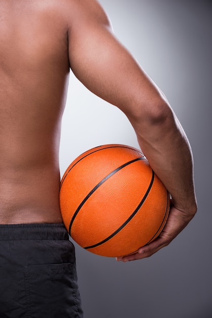 Pronto para jogar. Retrovisor de um homem africano sem camisa segurando uma bola de basquete