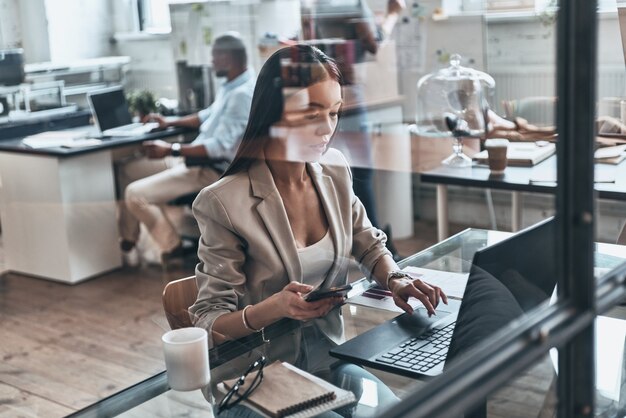 Pronto para trabalhar muito. Vista superior de uma jovem moderna usando o computador enquanto trabalha atrás de uma parede de vidro no escritório