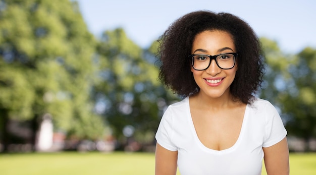 propaganda, educação, etnia, visão e conceito de pessoas - feliz sorridente jovem africana ou estudante adolescente em óculos e camiseta branca sobre o fundo do parque de verão