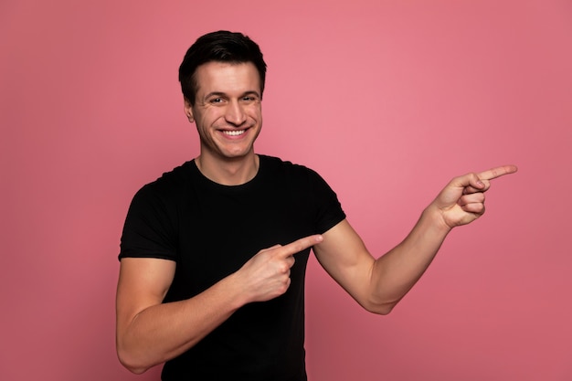 Foto propaganda. um homem atraente em uma camiseta preta, que está olhando para a câmera, sorrindo e apontando para a esquerda.