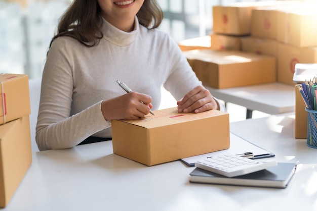 La propietaria de un negocio de ventas en línea está tomando nota de la dirección del cliente en la caja del paquete que se está preparando para la entrega