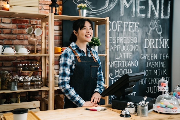 propietaria de una pequeña empresa con menú de cafetería en el fondo de la pizarra. joven camarera de pie en el mostrador saludando al cliente habitual en el café bar por la mañana. mujer en delantal sonriendo bienvenida