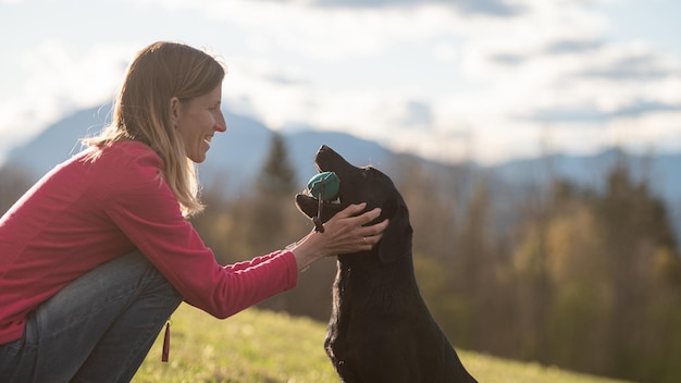 Propietario alabando amorosamente a su labrador retriever negro sosteniendo un maniquí