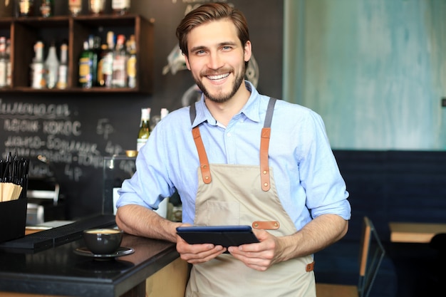 Propietario masculino joven con tableta digital mientras está de pie en la cafetería.