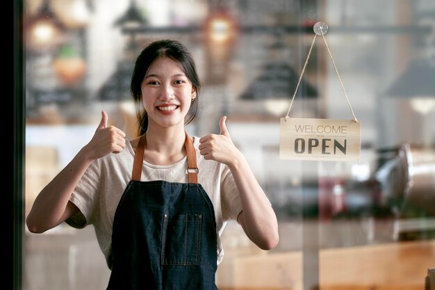 Propietario de negocio de café Concepto atractivo joven hermoso barista caucásico en delantal mostrando los pulgares hacia arriba y sonriendo a la cámara en la cafetería