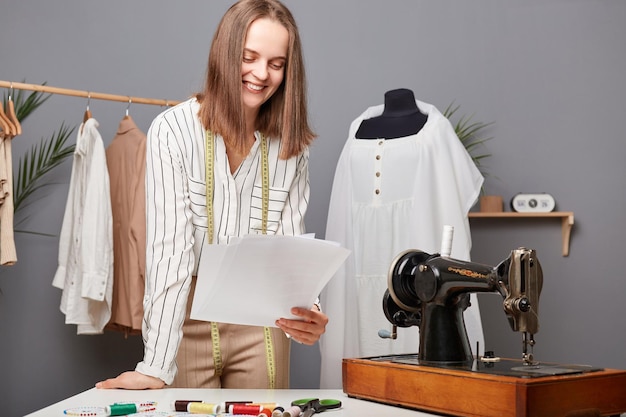 Foto propietario de una pequeña empresa de prendas de vestir diseñadora de moda caucásica sosteniendo papeles con bocetos en el taller pensando en nuevas ideas para el proceso de trabajo de costureras de vestidos