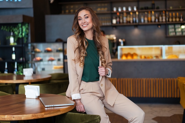 Propietario de restaurante de mujer de negocios con ordenador portátil en manos vestido elegante traje de pantalón sentado en la mesa en el restaurante con la superficie de la barra de bar Caucásico mujer de negocios interior