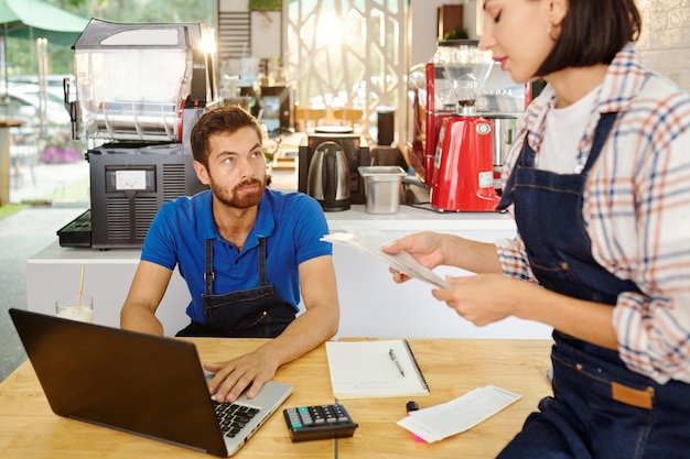 Propietarios de cafés serios jóvenes que controlan las facturas para analizar las ventas, los ingresos y los gastos