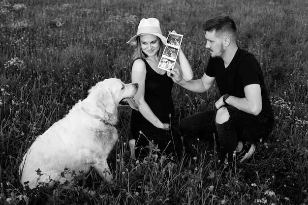 Los propietarios muestran una foto de ultrasonido a su perro, labrador blanco. Foto en blanco y negro. Esperando a un niño. Manejo del embarazo. Métodos modernos de examen Momentos felices del embarazo.