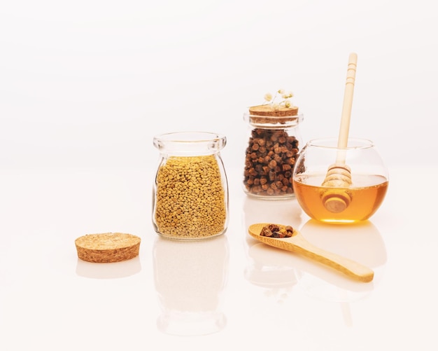 Propolis und Honig in Gläsern mit Honiglöffel auf einem weißen Tisch mit Reflexion und Kopierraum