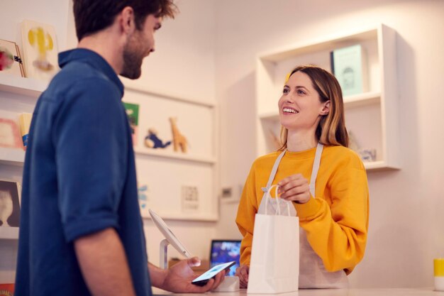 Proprietária de uma pequena empresa aceitando pagamento sem contato na loja do cliente usando telefone celular