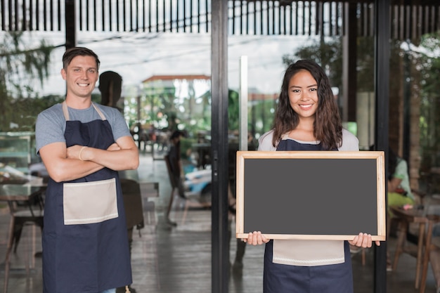 Proprietário de café masculino e feminino com orgulho em frente ao seu café ou cafeteria segurando uma lousa