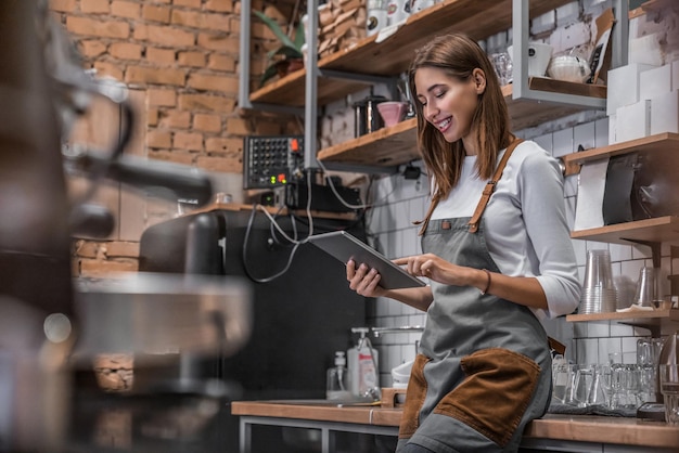 Foto proprietário de café sorridente em pé em seu local de trabalho perto do balcão e usando tablet digital