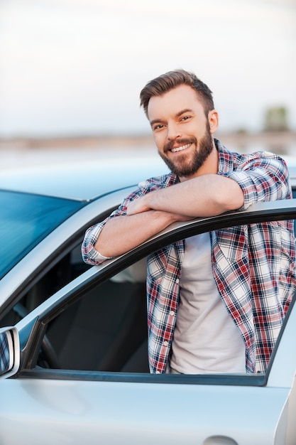 Foto proprietário de carro feliz. jovem feliz encostado na porta do carro e sorrindo para a câmera ao ar livre