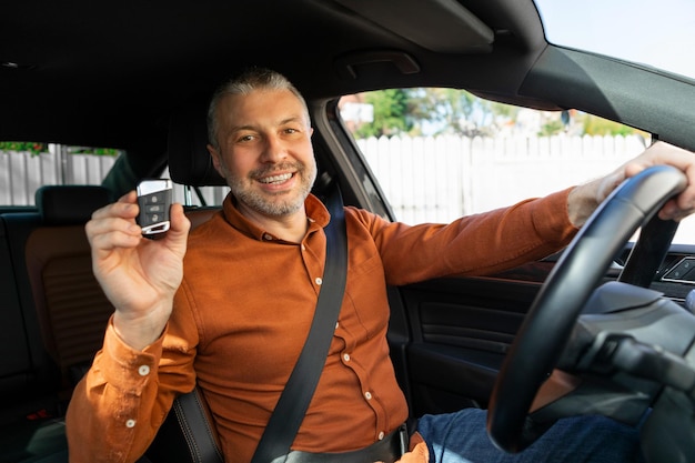 Proprietário de carro orgulhoso mostrando sua nova chave de carro enquanto dirige o veículo segurando a mão no volante