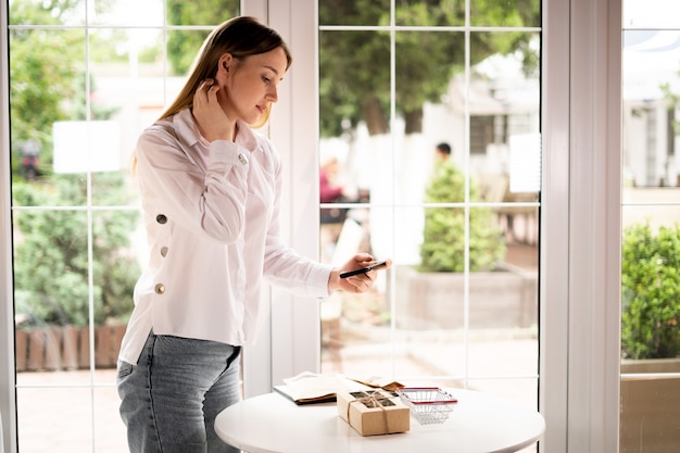 Proprietário de pequena empresa tira uma foto do produto em um café sobre a mesa. vista lateral de uma garota com um telefone. o vendedor, um empresário, tira fotos do produto para uma loja online.