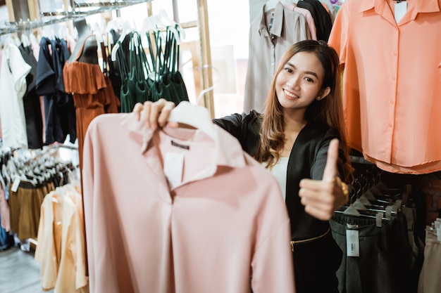 Proprietário em sua boutique em pé segurando roupas