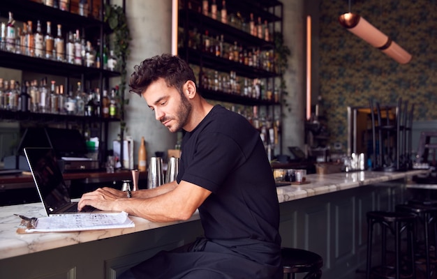Proprietário masculino do bar do restaurante sentado no balcão trabalhando no laptop