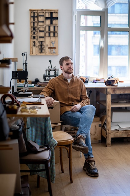 Proprietário masculino europeu sorridente de pequena empresa posando em oficina de couro curtidor profissional