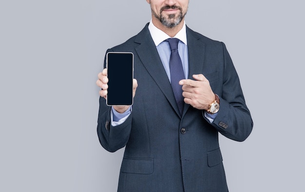 Propuesta de producto anuncio presentación copia espacio hombre que presenta la pantalla del teléfono chico recortado que muestra el teléfono inteligente sobre fondo gris hombre en traje formal señalando con el dedo en el dispositivo móvil