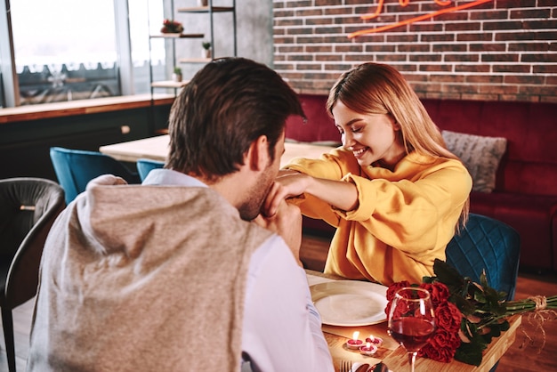 Propuesta romántica. Joven besa las manos de su novia en el restaurante. Rosas rojas y velas están sobre la mesa cerca del vino tinto. Foto recortada, primer plano