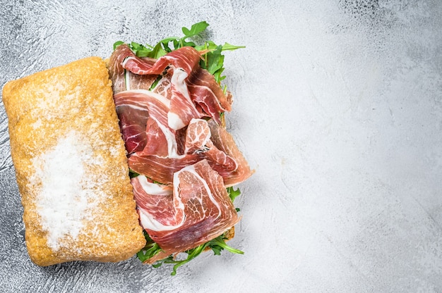 Prosciutto-Parmaschinken-Sandwich auf Ciabatta-Brot mit Rucola. Weißer Hintergrund. Ansicht von oben. Platz kopieren.