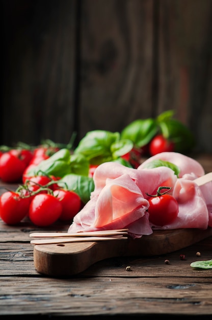 Prosciutto tradicional italiano con tomate y albahaca sobre la mesa de madera