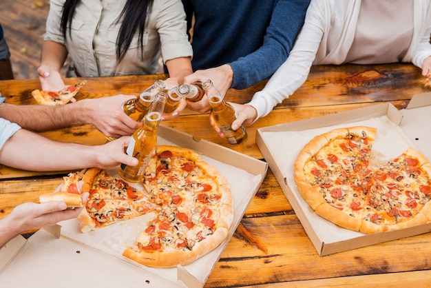 Prost auf dieses Wochenende! Draufsicht einer Gruppe junger Leute, die Flaschen mit Bier halten und Pizza essen, während sie im Freien stehen standing