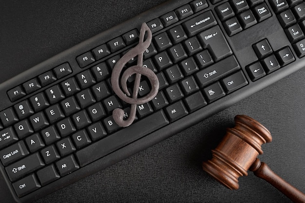 Foto proteção da música como propriedade intelectual. clave de sol no teclado ao lado do martelo de madeira em fundo preto. licenciamento de música.