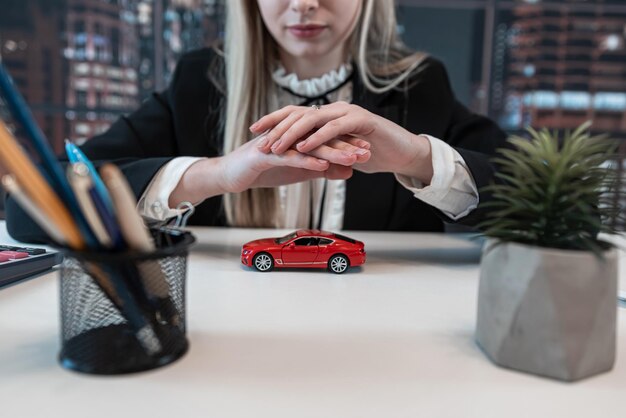 Foto protección del automóvil mujer de negocios sostiene un pequeño vehículo rojo de juguete en su mano para el seguro en la oficina concepto de seguro de viaje