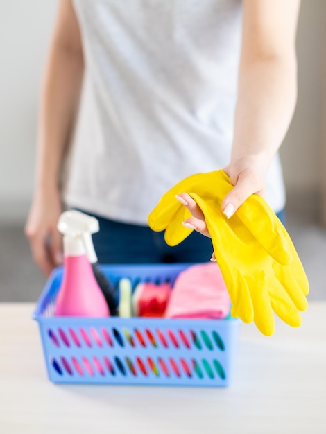 Protección para el cuidado de la piel Tareas domésticas Equipo de ama de casa Mujer irreconocible que ofrece guantes amarillos que se quedan con herramientas de limpieza de cestas en el desenfoque de la mesa