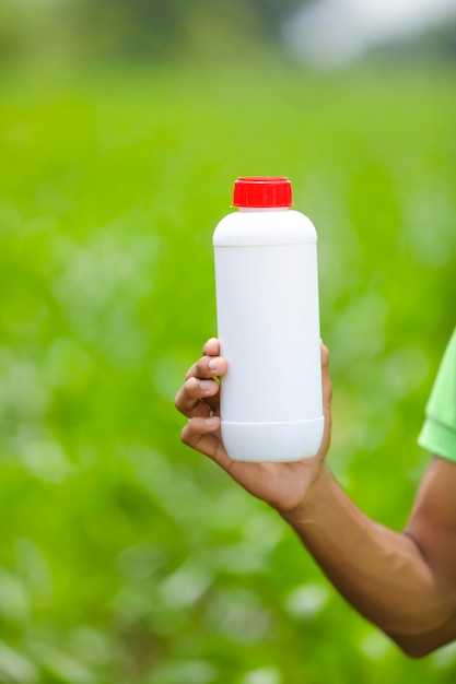 Protección de cultivos contra plagas y enfermedades. mano que sostiene la botella de pesticida en el campo de la agricultura.