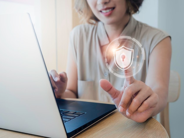 Foto protección de datos personales de seguridad cibernética y concepto de privacidad comercial icono de escudo y candado en el aire mientras la mujer escanea con el dedo para identificar el acceso mientras usa una computadora portátil