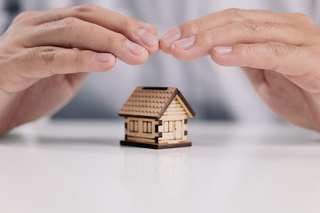 Protección de manos sobre la casa en el escritorio, la seguridad del hogar y el concepto de seguro