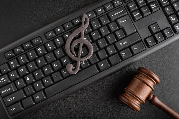 Protección de la música como propiedad intelectual. Clave de sol en el teclado junto al mazo de madera sobre fondo negro. Licencias de música.