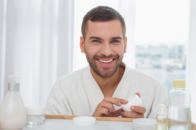 Foto protección de la piel. buen hombre alegre sosteniendo una botella de crema mientras se preocupa por su piel