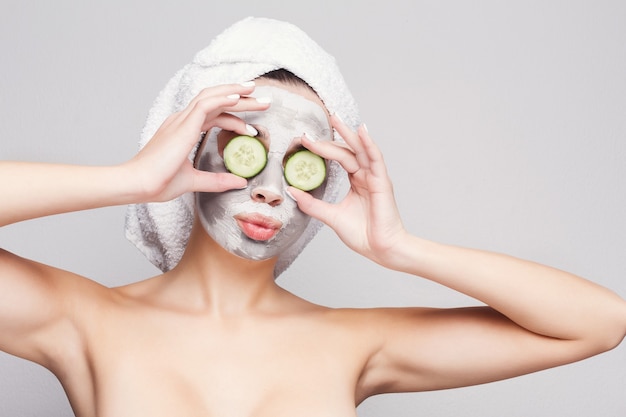 Protección de la piel. Hermosa chica con máscara de colágeno y rodajas de pepino en los ojos contra el fondo gris obteniendo un tratamiento de belleza. Concepto de spa con espacio de copia