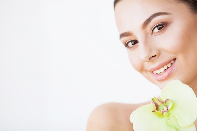 Protección de la piel. Hermosa mujer modelo con piel perfecta y flor de orquídea cerca de su cara