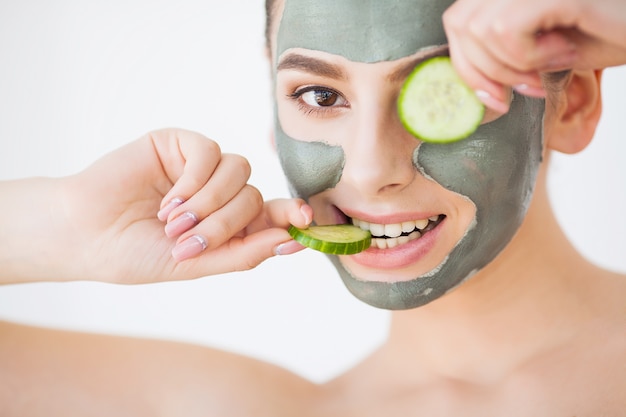 Protección de la piel. Mujer joven con máscara de arcilla cosmética con pepino en su baño