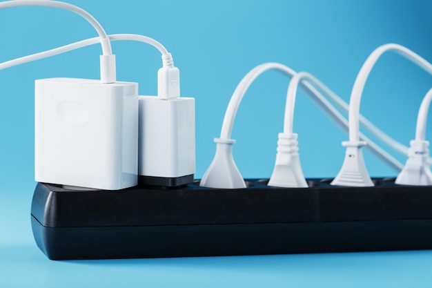 Protector contra sobretensiones con cables blancos conectados de aparatos eléctricos sobre un fondo azul. Espacio libre