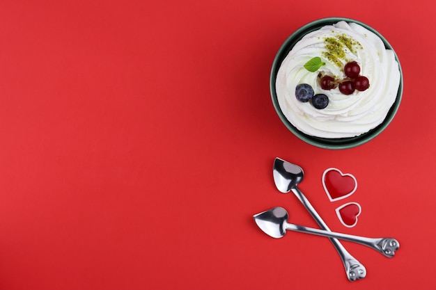 Protein-Cupcake mit Beeren und Minzblatt auf rotem Hintergrund mit herzförmigen Löffeln in der Nähe