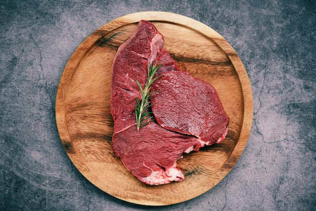 Proteína animal de res fresca / carne de res cruda con romero blanco en un plato de madera en la cocina para cocinar filete de res asado oa la parrilla con ingredientes hierba