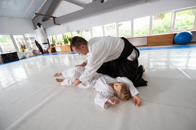 Proteja-se. Treinador de aikido de cabelos escuros vestindo quimono, ensinando menino a se proteger